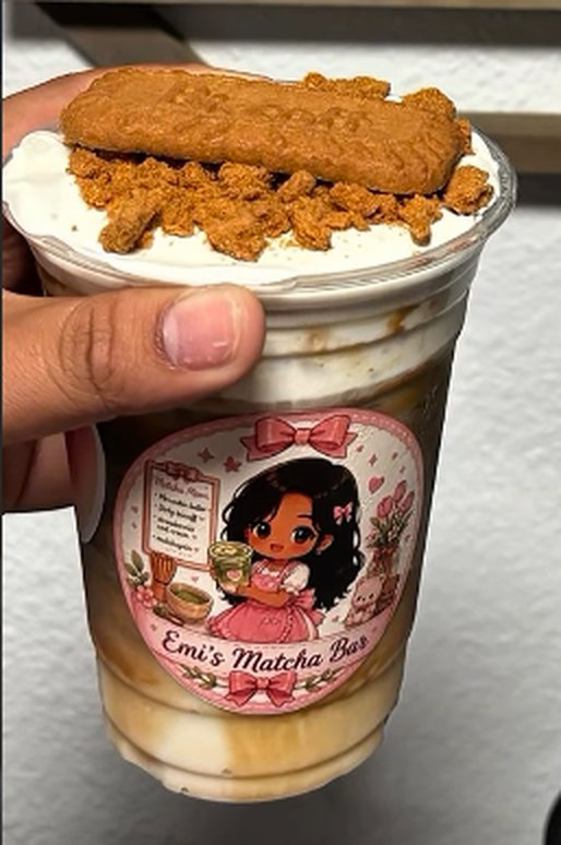 A hand holding an Emi's Matcha Bar drink topped with cold foam and a Biscoff cookie